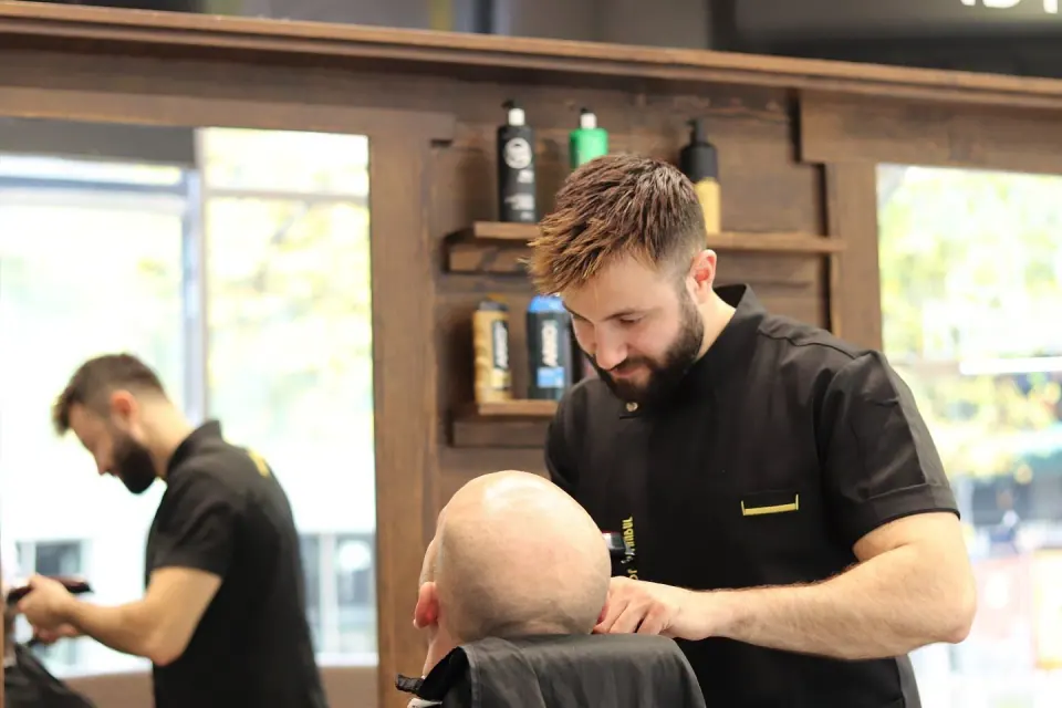 Two barbers at work in the shop, wooden shelves of products behind them
