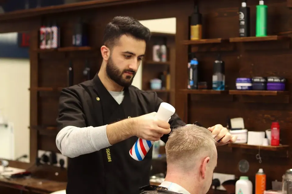 A barber misting a customer's hair while cutting it